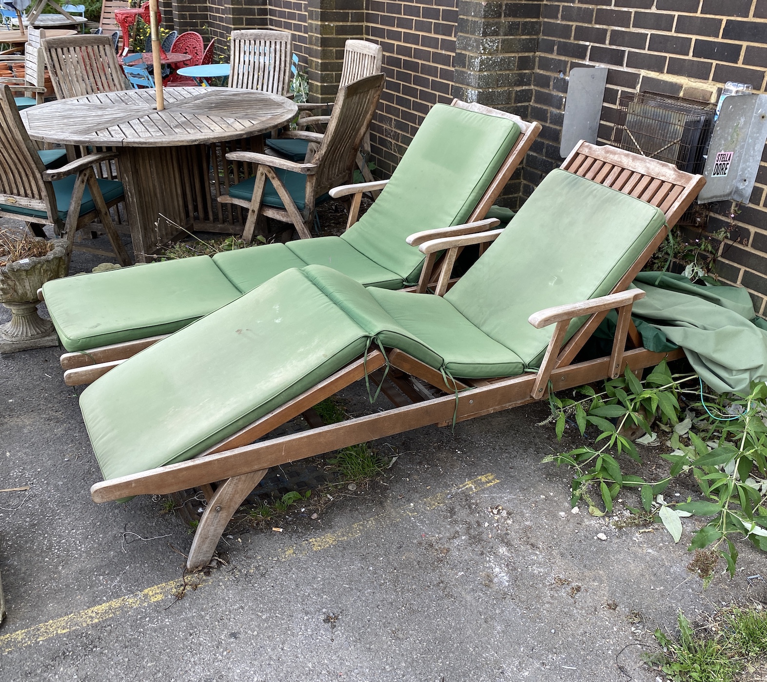 A pair of weathered teak garden loungers with seat cushions and rain covers